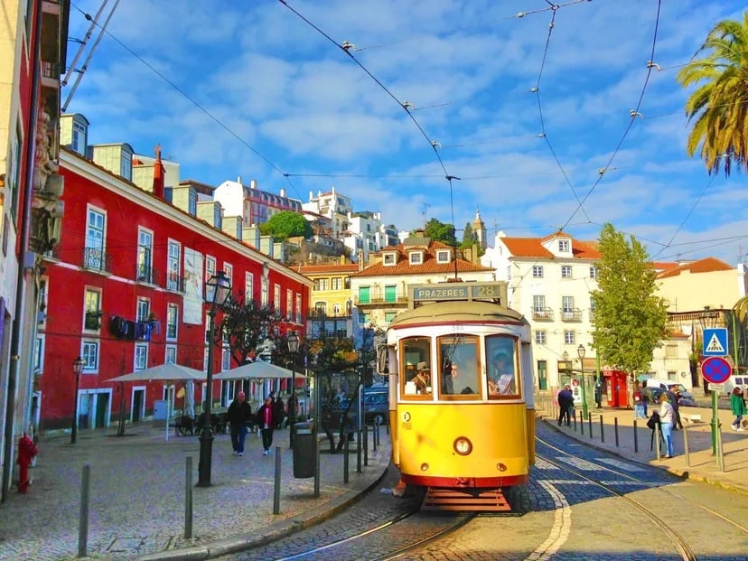 Yellow Lisbon tram on a cobbled street lined with colorful buildings and overhead wires.