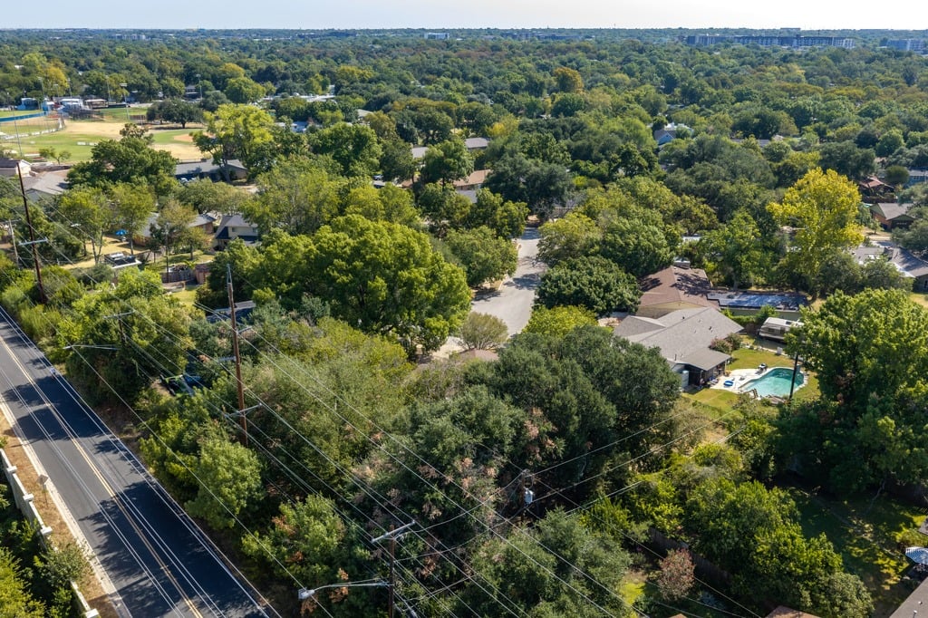 Aerial view of a leafy neighborhood, with homes, a roadside, and a backyard pool.
