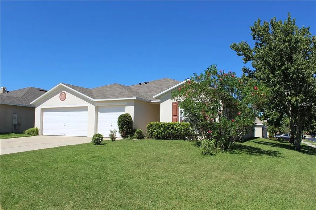 Home exterior with two garage doors, a broad green lawn, and flowering shrubs.