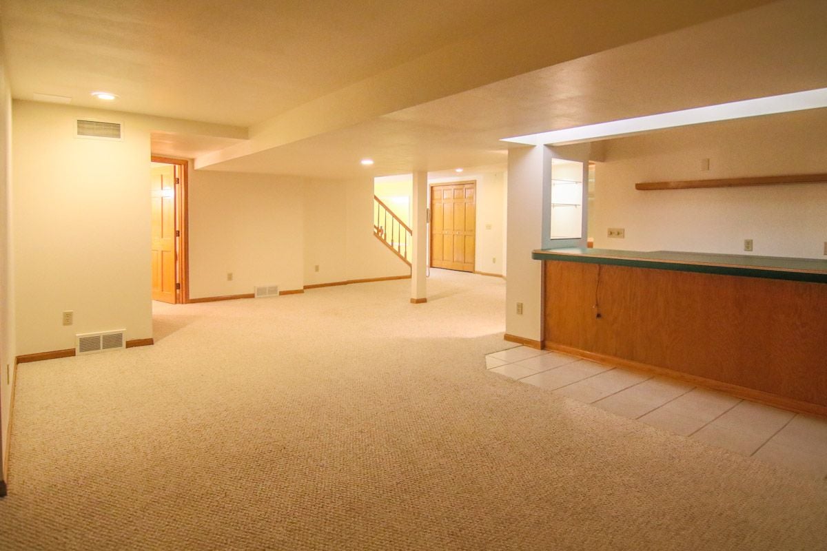 Finished basement with beige carpet, a wood-paneled wet bar, and a staircase.