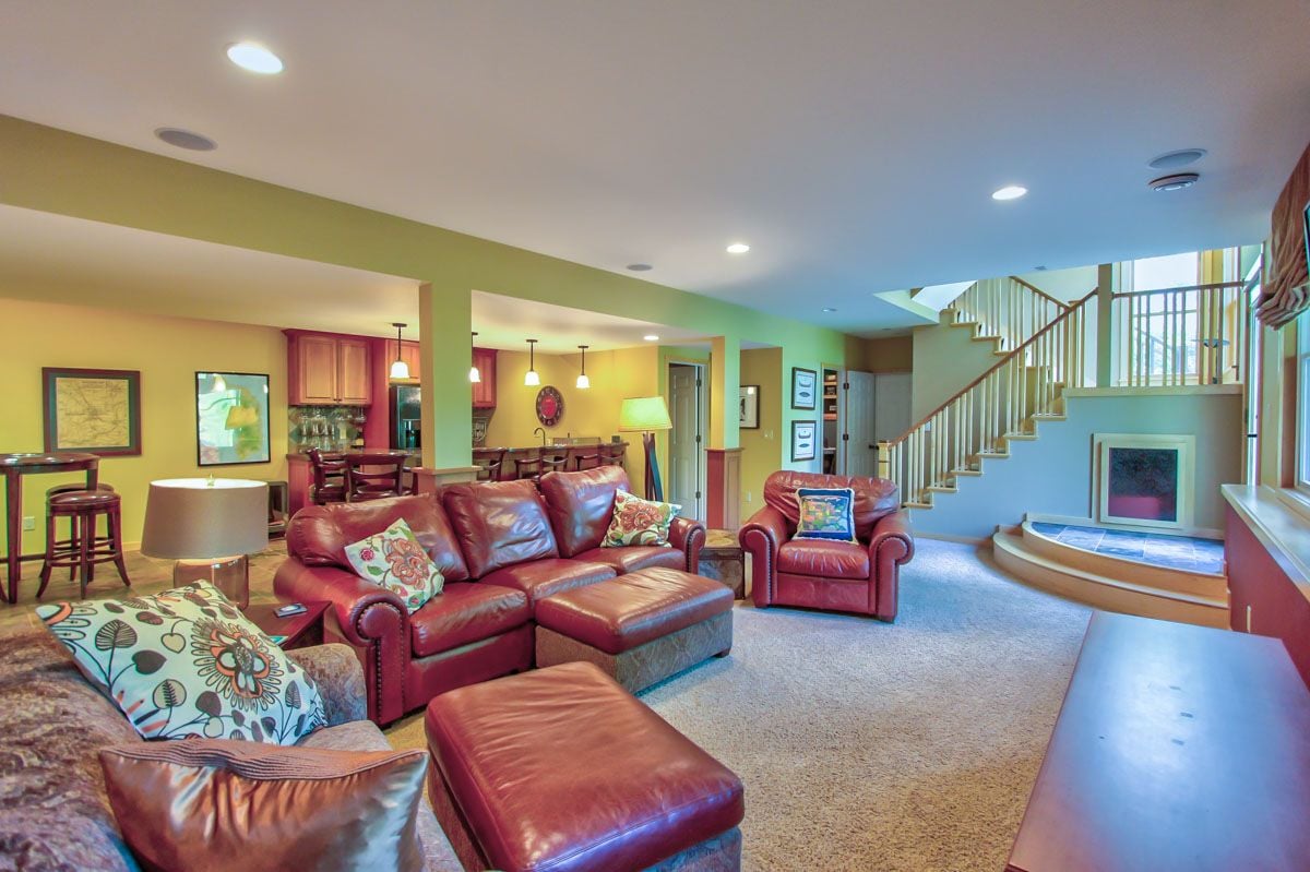 Living room with red leather seating, an open kitchen, staircase, and fireplace.