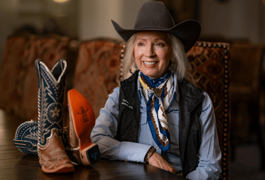 Woman in a cowboy hat seated beside ornate western boots.