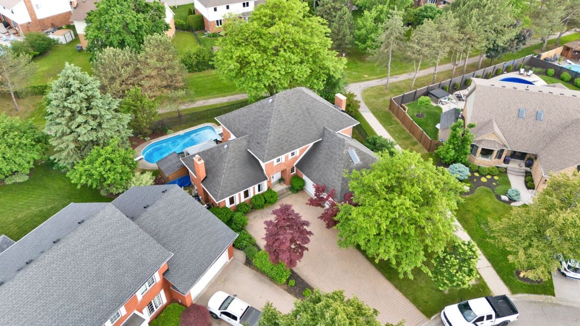 Aerial view of a red-brick home with a backyard pool and mature trees.