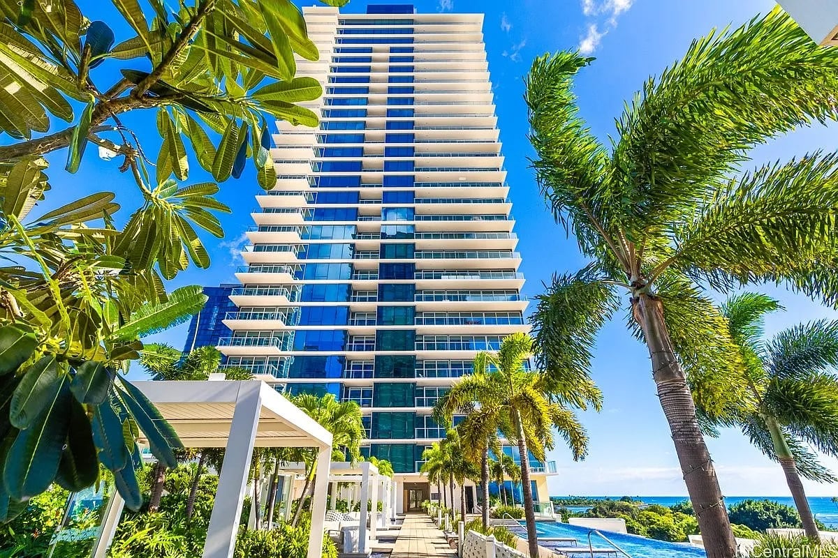 Modern high-rise condominium framed by palms, with a pool and ocean visible beside it.