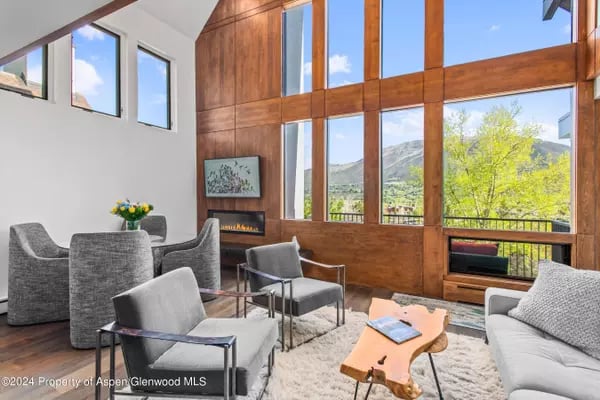 Living room with tall wood-framed windows overlooking mountains and green trees.