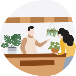 Two people arrange potted houseplants on a counter, with a hanging plant above them.
