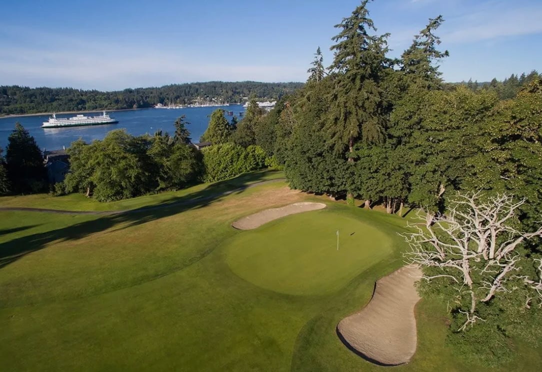 Wing Point golf course green and sand bunkers overlooking a wooded shoreline and ferry crossing the water.