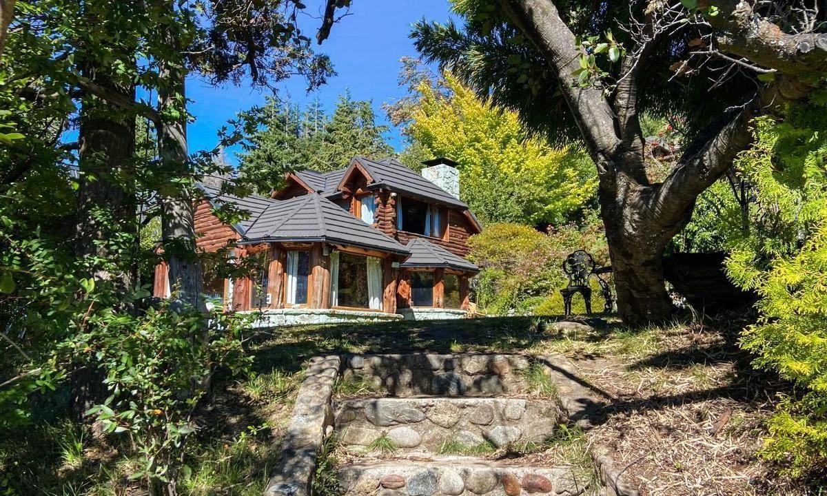 Rustic log cabin among mature trees, reached by stone steps through a leafy garden.