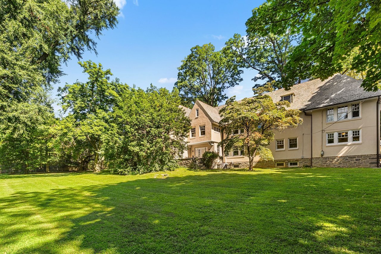 Large beige house behind a broad lawn, framed by mature trees.