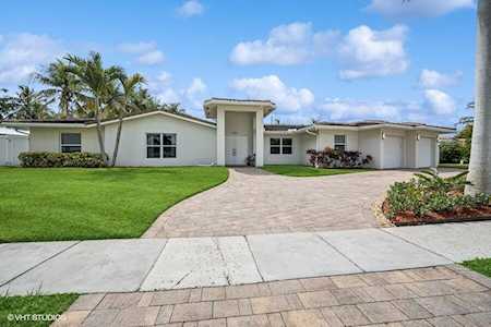 Single-story home with a curved paver driveway, front lawn, palm trees, and attached garage.