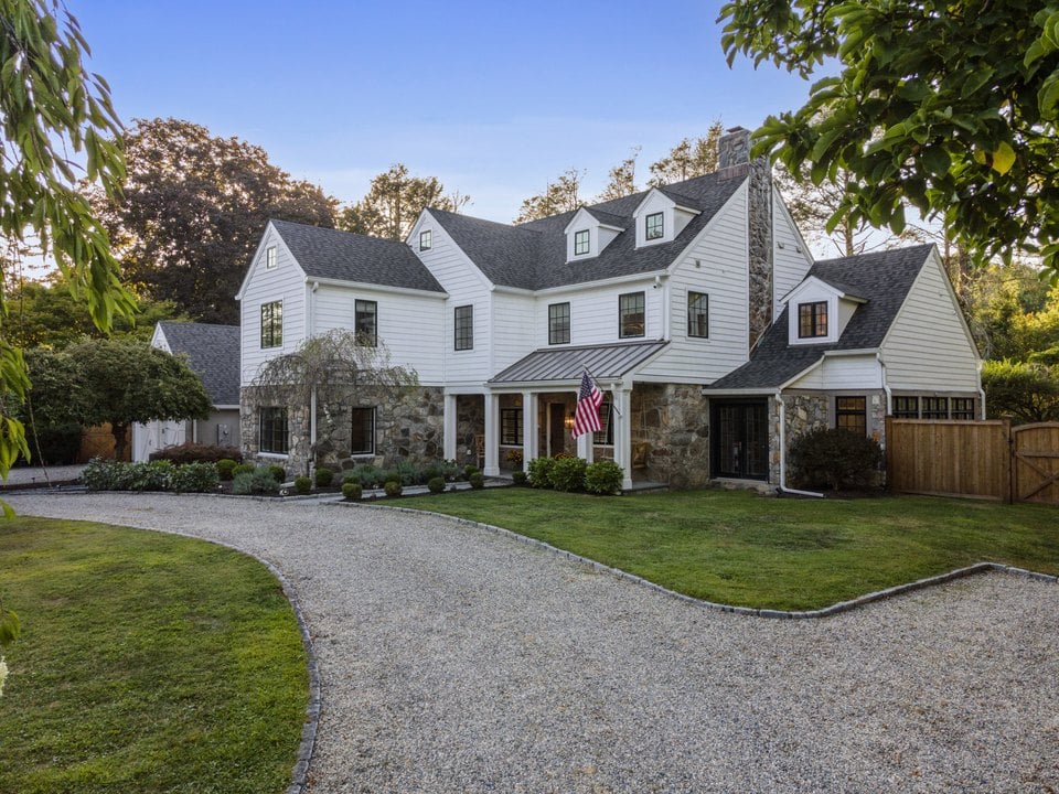 White two-story house with stone accents, multiple gables, and a curved gravel driveway.