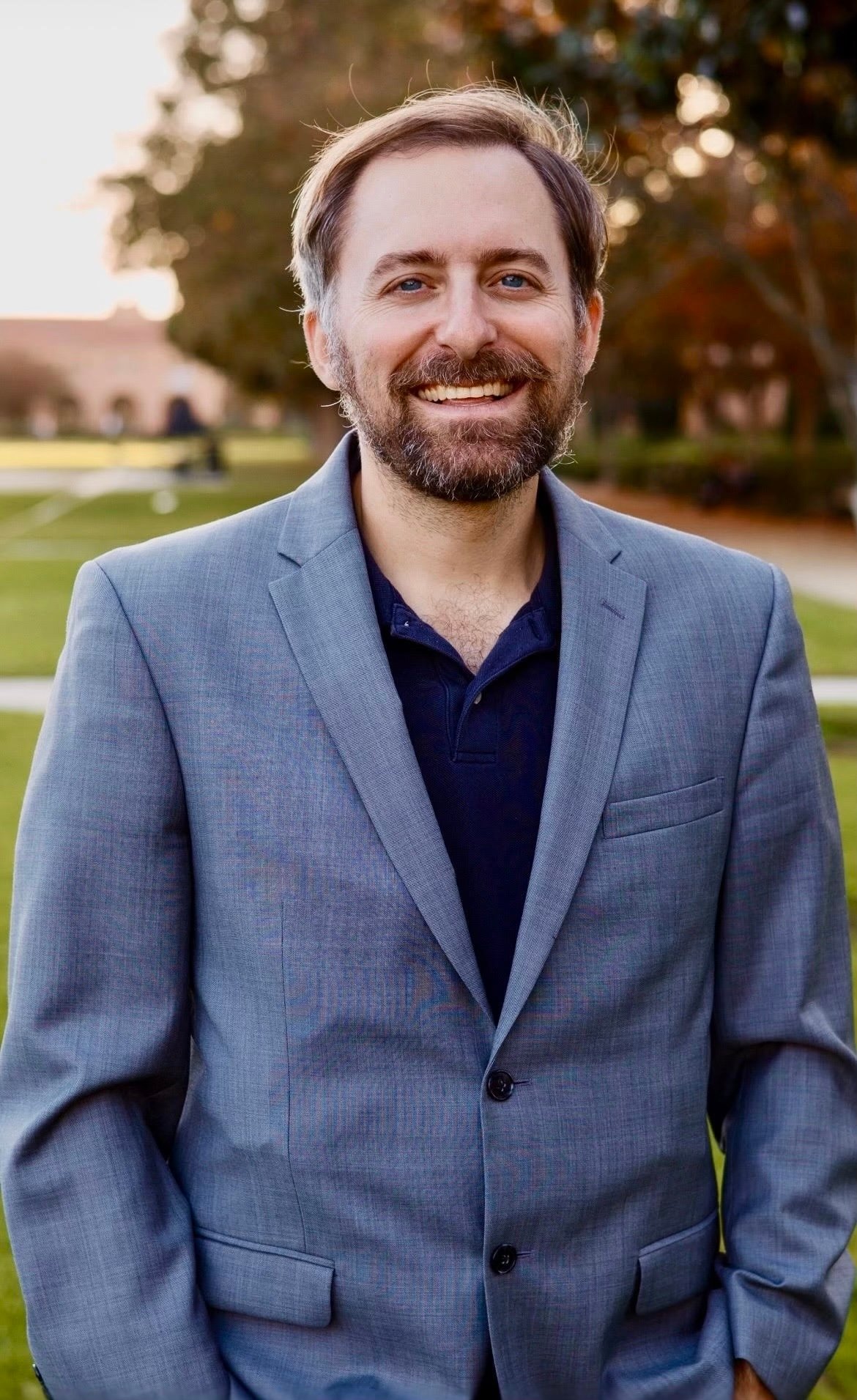 Max Lemanowicz smiling in a blue-gray blazer outdoors.