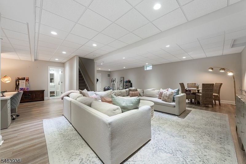 Finished lower-level living room with white sectional sofas, exercise equipment, and a dining area.