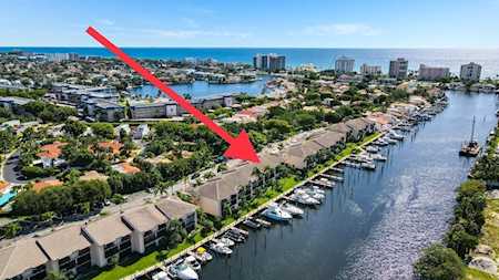 Aerial view of waterfront homes beside a marina canal, marked by a red arrow.