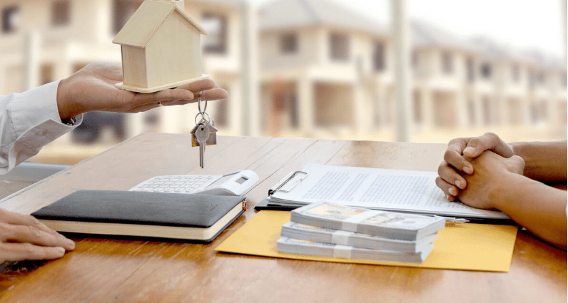 A model house and keys are presented across a table with real estate paperwork.