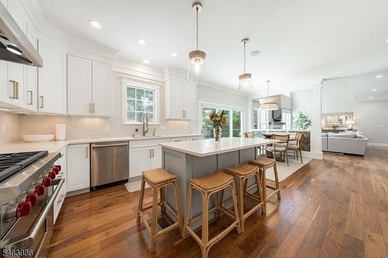 Open-plan kitchen with a large island, woven bar stools, white cabinetry, and hardwood floors.