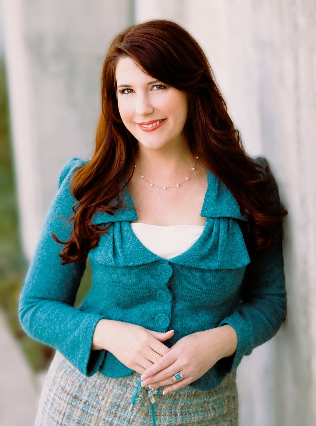 Christina Crump in a teal cardigan, wearing a pearl necklace and clasping her hands.