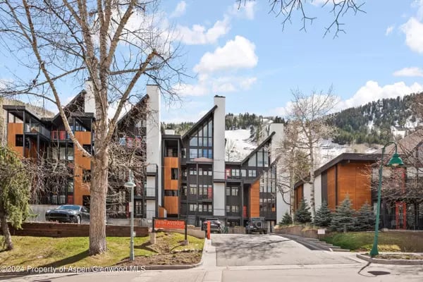 Modern condominium buildings with orange-brown accents, leafless trees, and a snow-covered mountain backdrop.