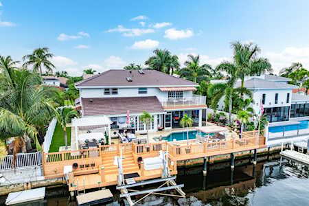 Two-story waterfront home with a wooden dock, pool, palm trees, and canal.