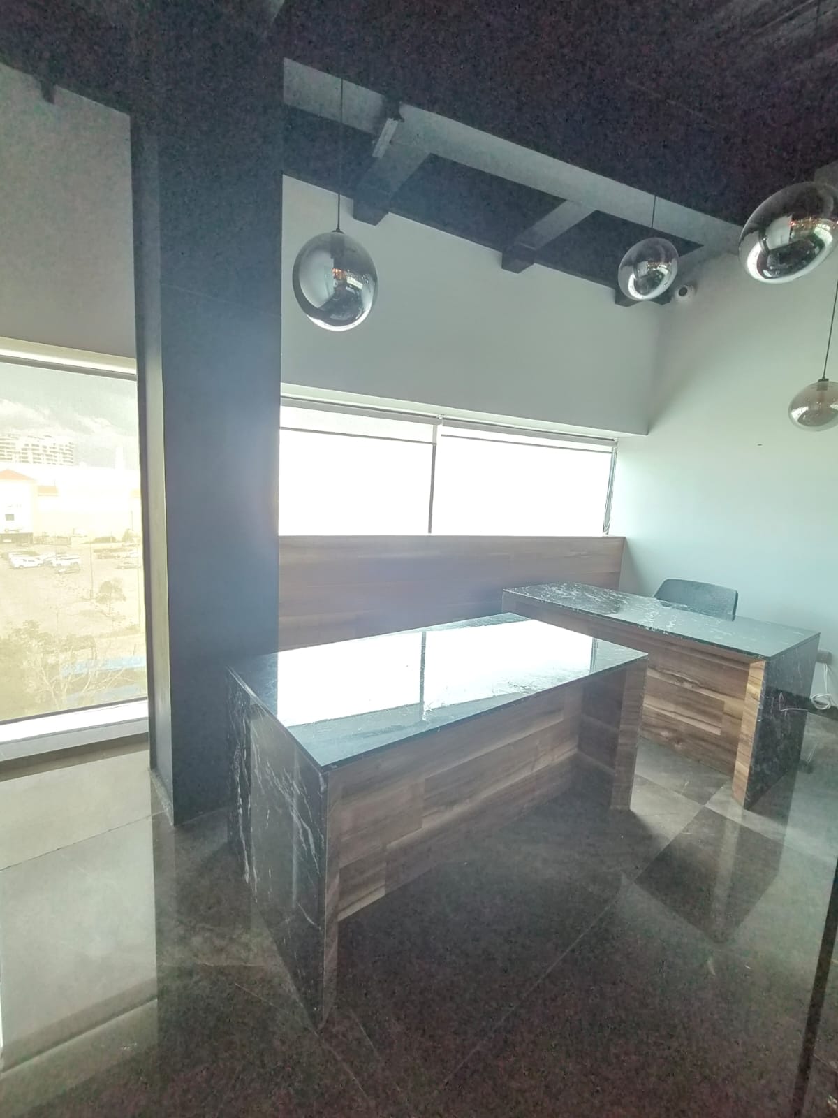 Office reception desk with wood panels and dark stone counters beneath reflective pendant lights.