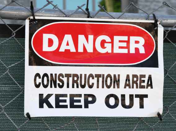 Construction area warning sign on a chain-link fence, marked “DANGER” and “KEEP OUT.”