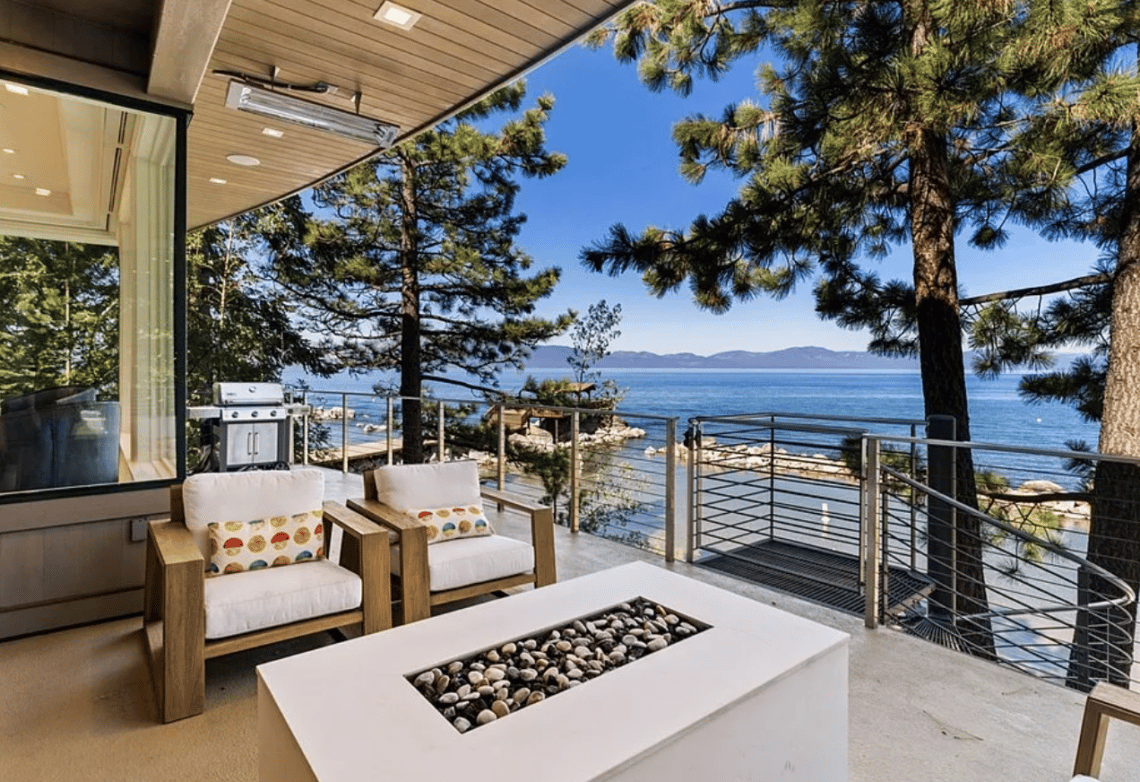 Lakefront patio with cushioned chairs, a stone-filled fire table, and views across Lake Tahoe.