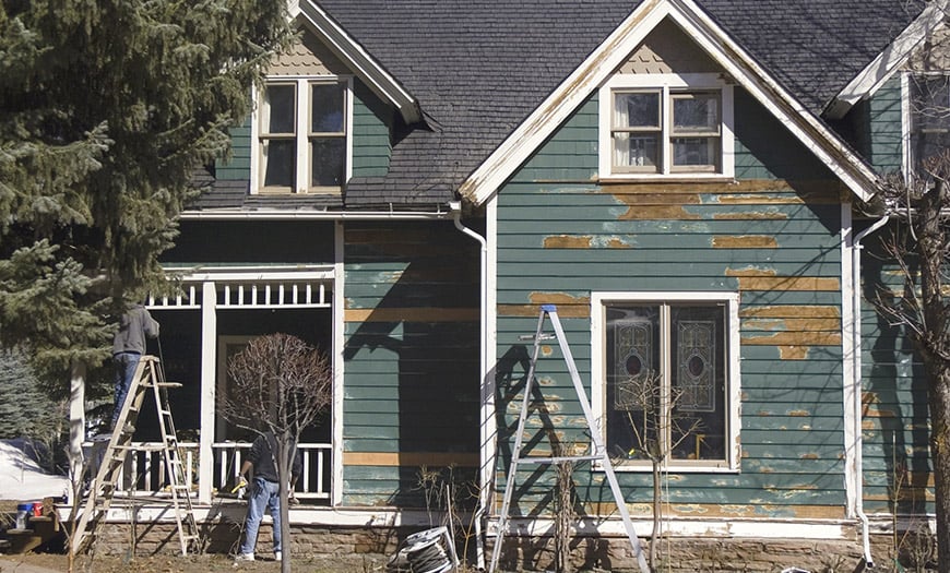 Green house exterior under renovation, with peeling siding and ladders.