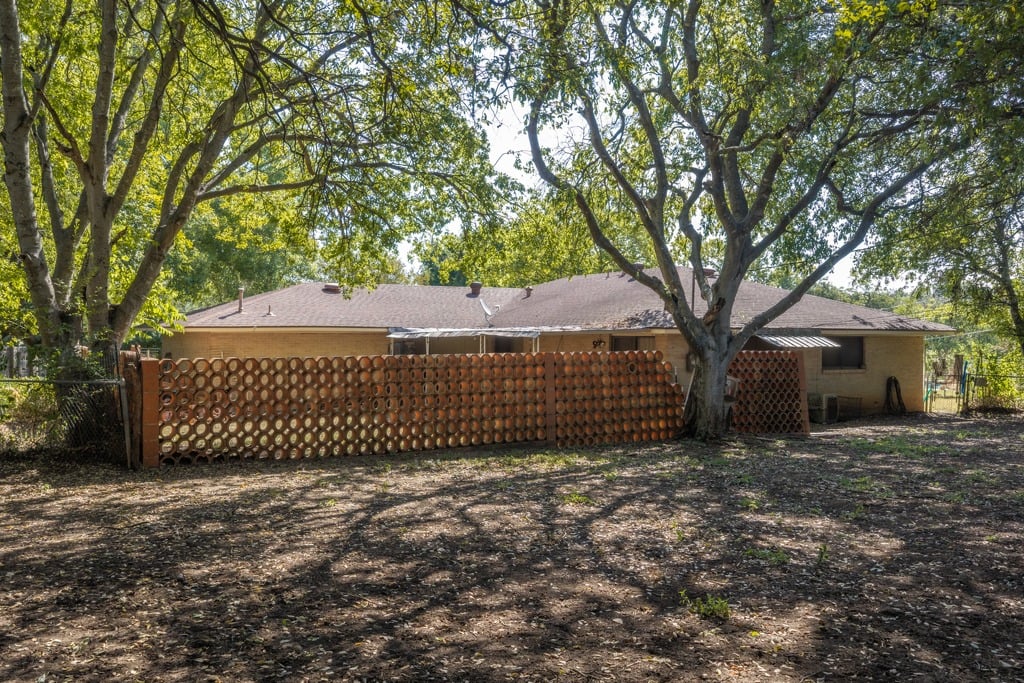 Single-story house behind a long wooden lattice fence, shaded by mature trees.