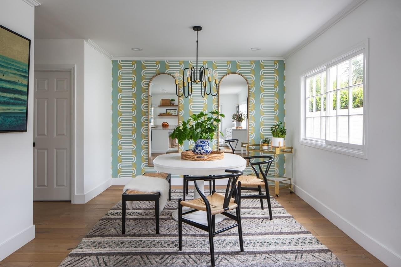 A dining room with a white oval table, a geometric patterned rug, and a light blue and gold patterned accent wall.