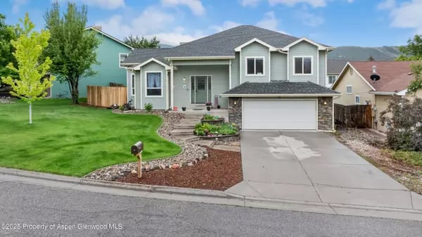 Two-story gray house with a double garage, broad driveway, and landscaped front lawn.