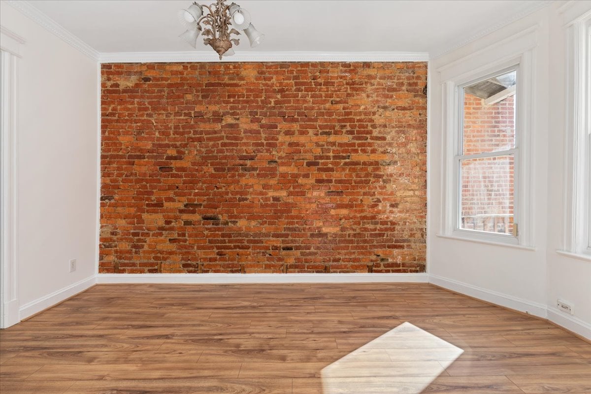 Vacant room with an exposed brick wall, wood flooring, and tall windows.