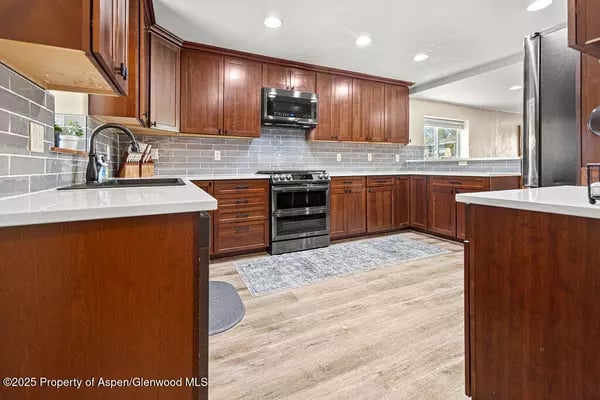 Kitchen with dark wood cabinets, gray tile backsplash, and stainless steel appliances.