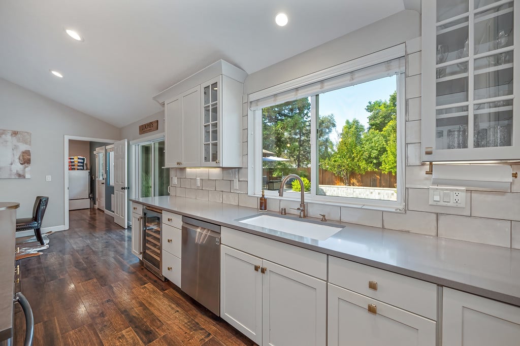 Kitchen with white cabinetry, a sink beneath a large window, and dark wood flooring.