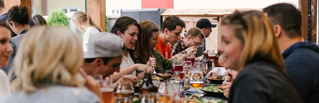 Friends and family share a crowded meal at a long restaurant table.