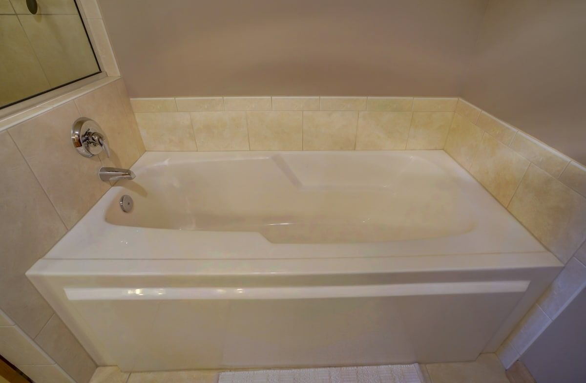 Built-in white bathtub with chrome fixtures and beige tile surround.