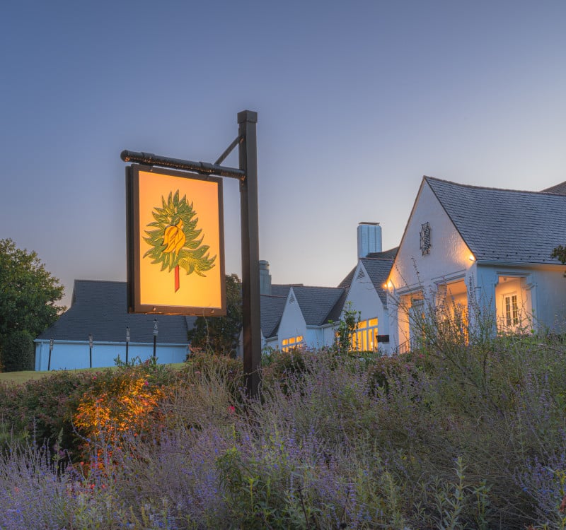 Hope Valley Country Club clubhouse at dusk, with a glowing sign and flowering landscaping.