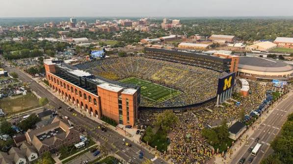 Aerial view of Michigan Stadium with a crowded football field and surrounding streets.