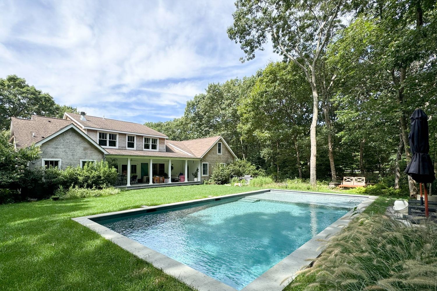 Two-story home behind a rectangular swimming pool, with a covered patio and mature trees.