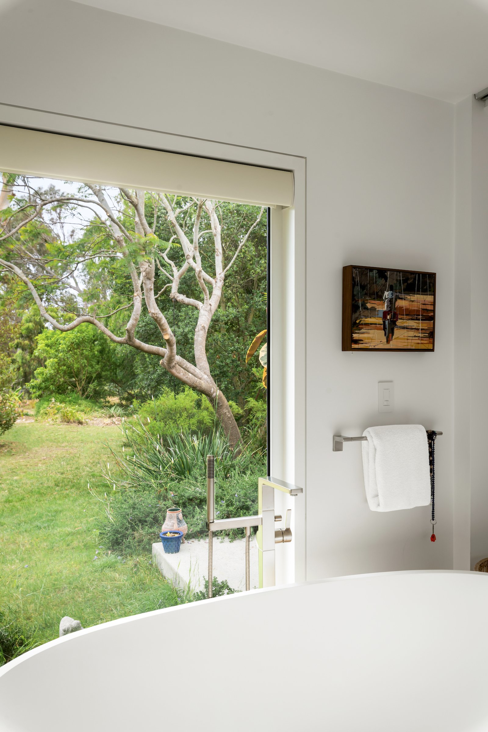 Freestanding bathtub beside a large window overlooking a leafy garden.