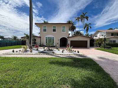 Two-story house with a dark garage, broad driveway, landscaped entry, and palm trees.