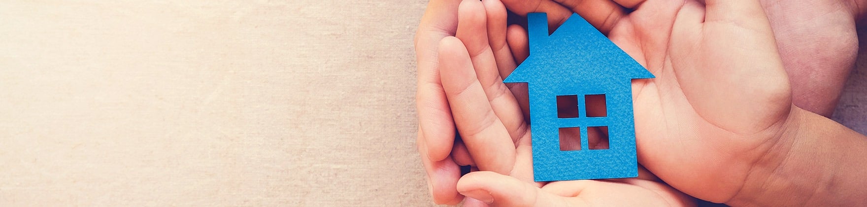 Hands hold a bright blue cutout house.