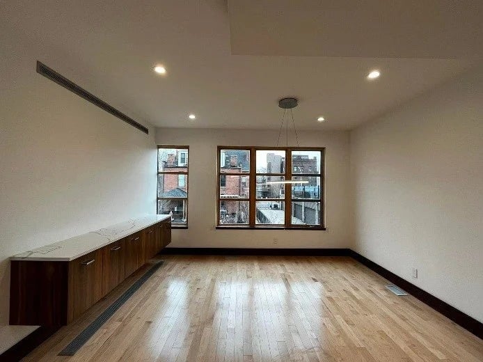 Empty interior room with a long wood cabinet, light wood floors, and large windows.