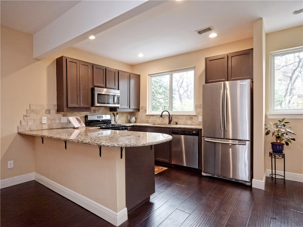 Kitchen with a granite peninsula, dark wood cabinets, and stainless steel appliances.