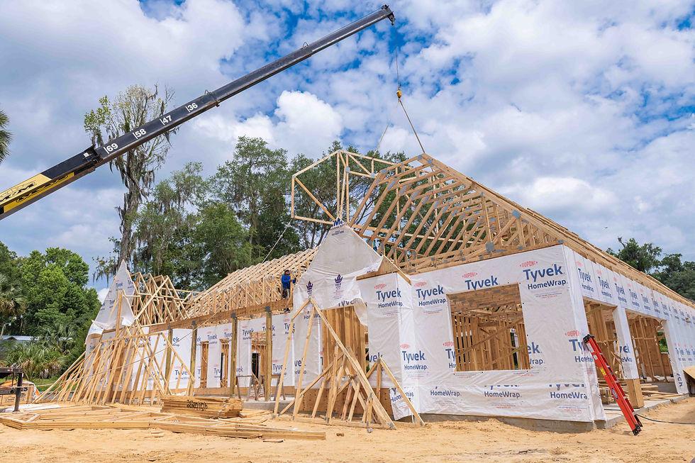 House under construction as a crane lifts roof trusses above its timber frame.