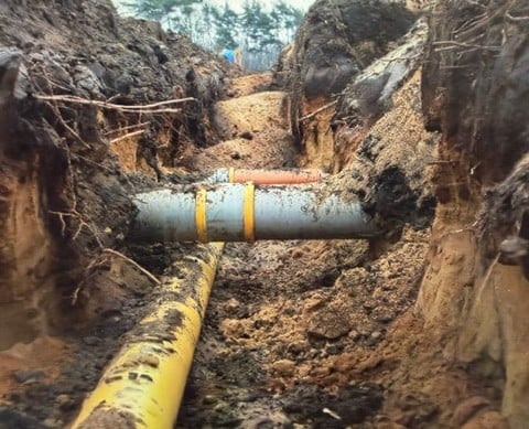 Yellow and gray pipes crossing an excavated trench.