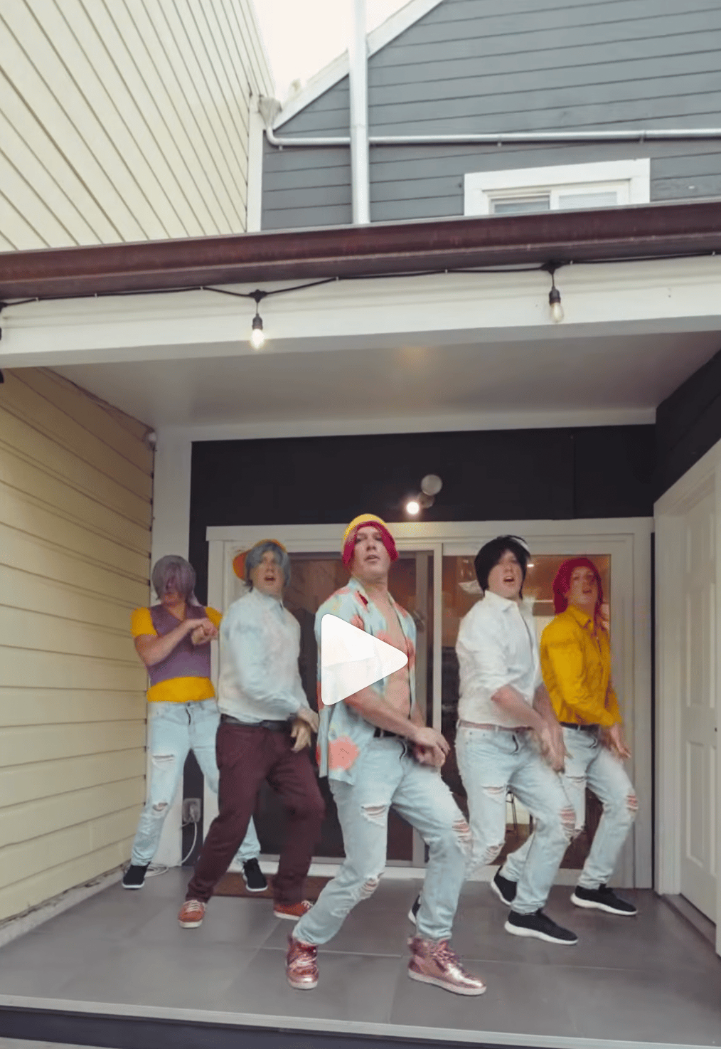Five costumed dancers perform on a covered porch in front of sliding glass doors.
