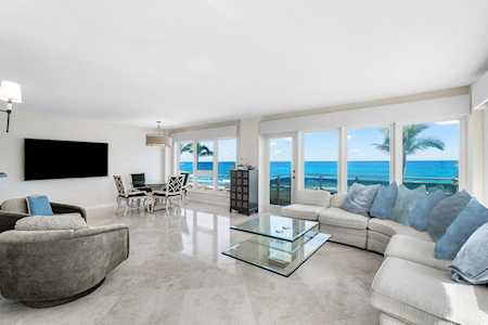 Open-plan living and dining room with pale sofas, polished floors, and ocean views through large windows.