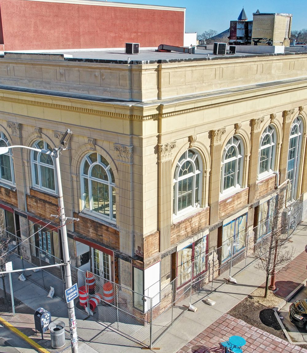 Cream-colored building with ornate arched windows and construction fencing along the sidewalk.