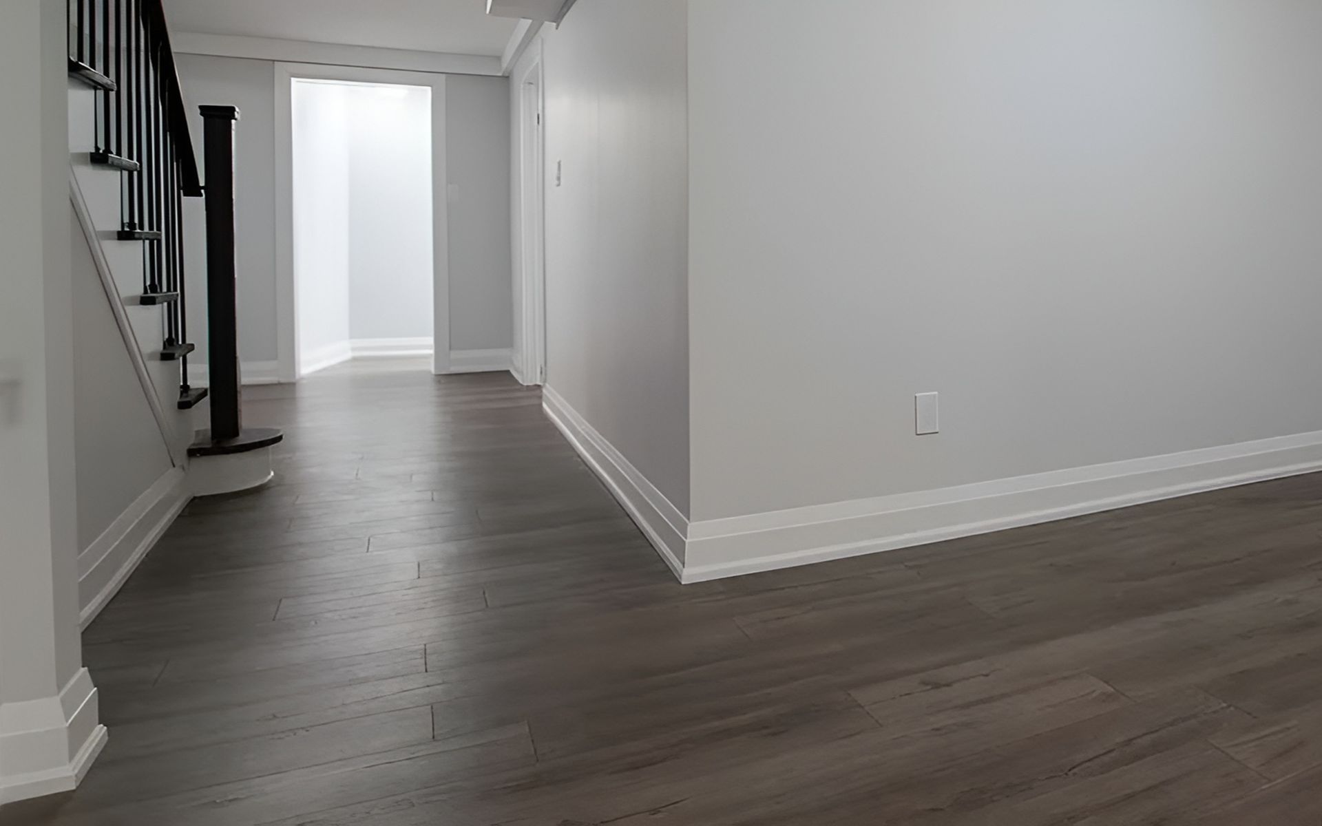 Empty hallway with dark wood-look floors and a staircase with black railings.