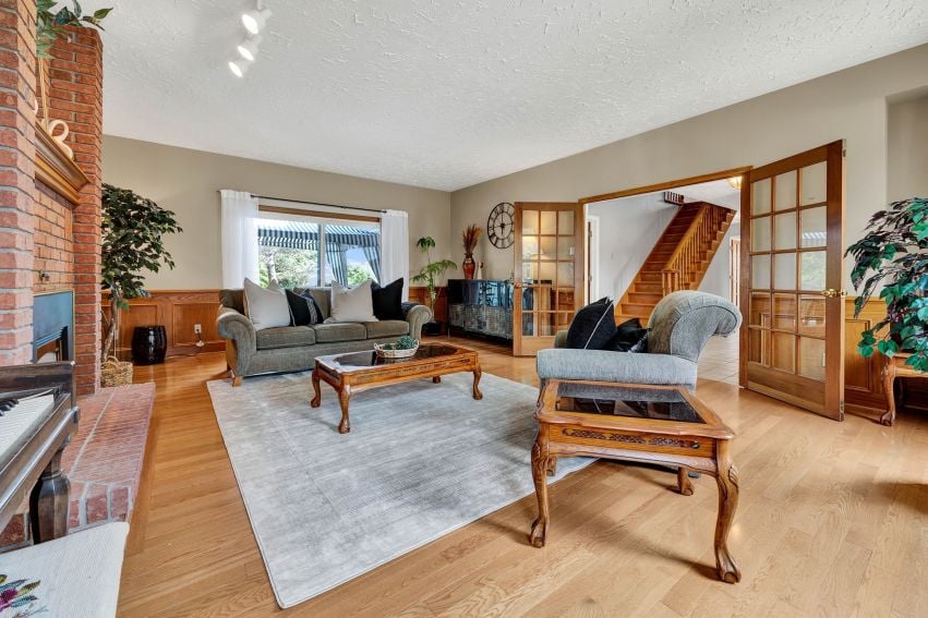 Living room with a brick fireplace, hardwood floors, and glass-paneled doors opening toward a wooden staircase.